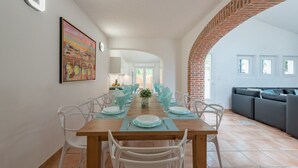 Un comedor con una mesa de madera dispuesta para seis personas, sillas blancas y un cuadro grande en la pared.