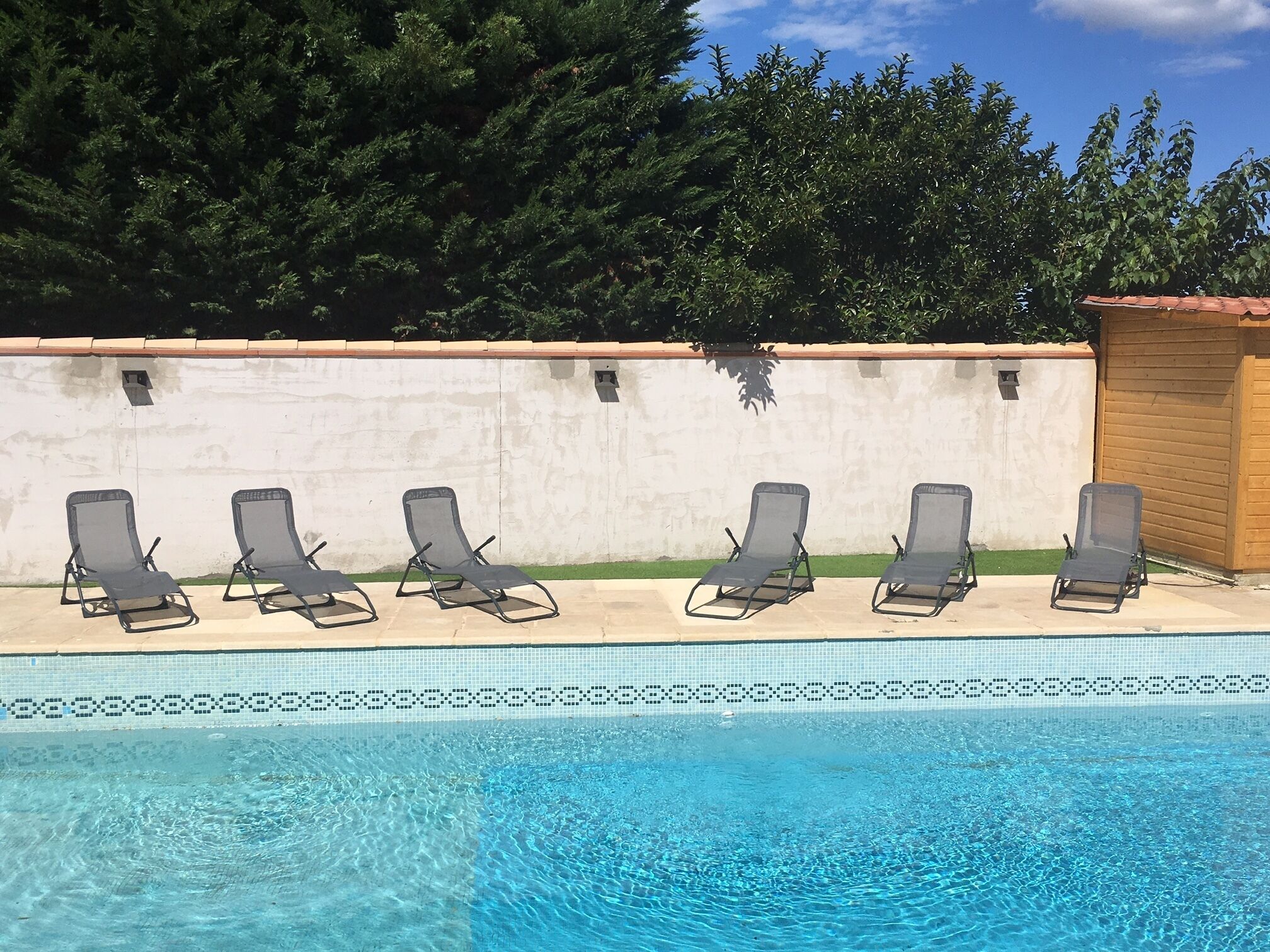 A swimming pool with six lounge chairs aligned along the edge.