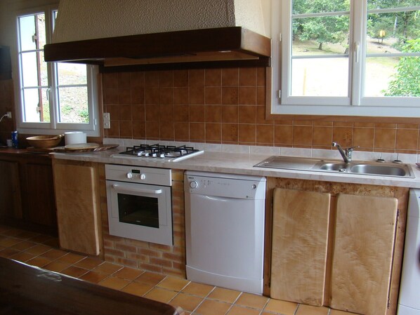 A kitchen with a gas stove, oven, dishwasher, and a window with a view of greenery.