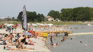 Una playa concurrida con gente tomando el sol, nadando y barcos en el agua.