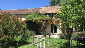 Una casa rústica con techo de tejas, rodeada de un jardín cuidado con diversas plantas y un portón de madera.