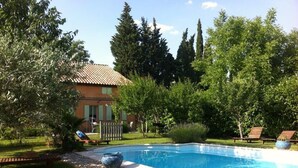 Una piscina rodeada de un jardín, con una casa al fondo.