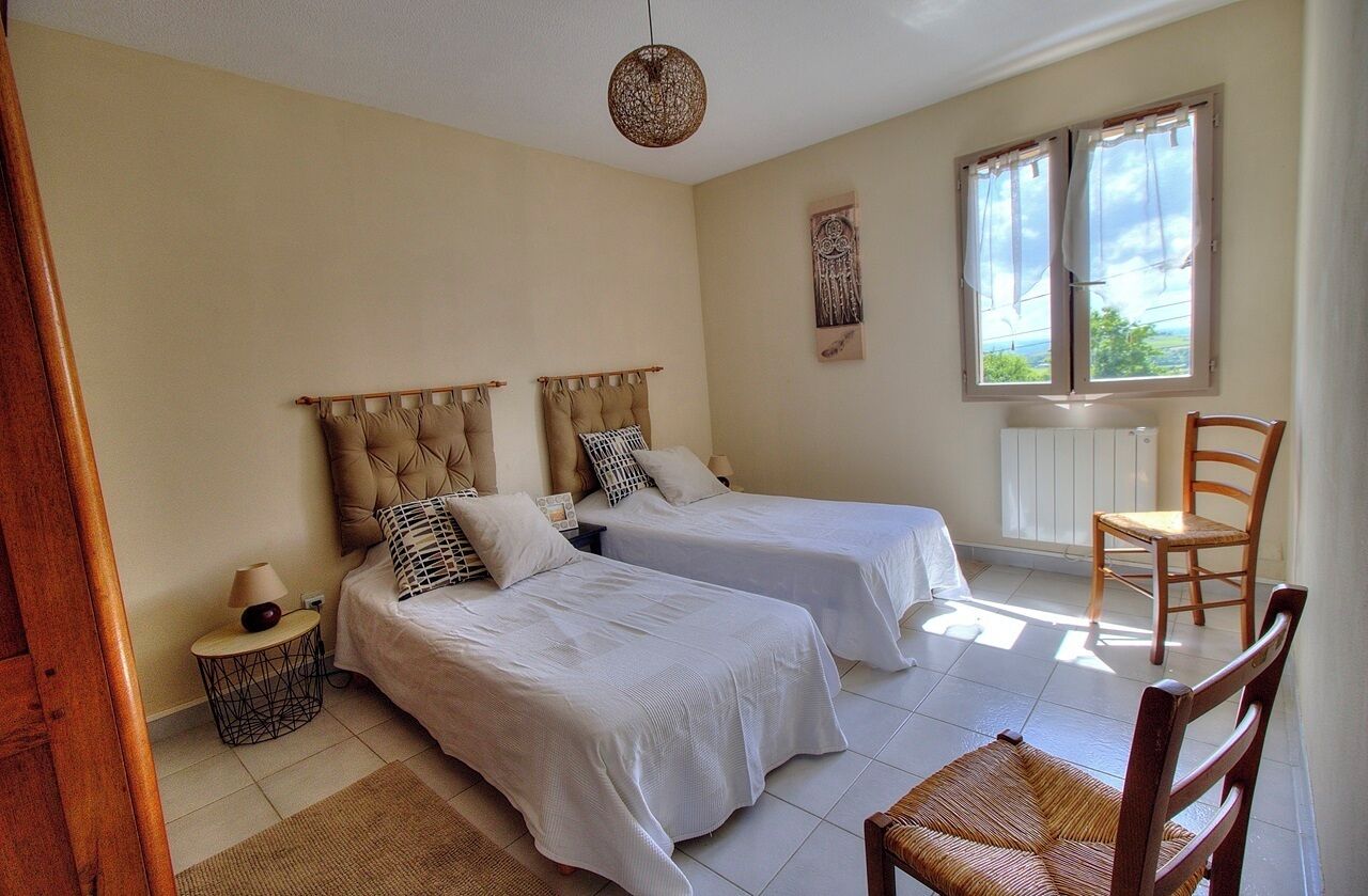Une chambre avec deux lits, une chaise, une table de chevet, une fenêtre avec des rideaux et un élément décoratif mural.