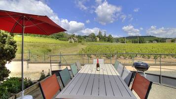 Un espace de restauration en plein air avec une table, des chaises, un parasol rouge et une vue sur un vignoble.