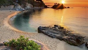Ein Strand mit klarem Wasser, einem Sonnenuntergang und Felsen.