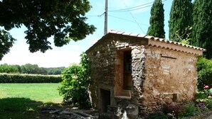 Un edificio rústico de piedra con techo de tejas, rodeado de un jardín con flores y un campo de césped al fondo.