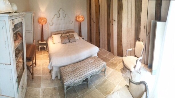 A bedroom with a bed, bench, bedside table, lamp, and a chair.