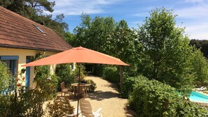 A patio with a table and chairs, a red umbrella, and a pool area. - Comfortable cottage in a wooded area by the pool near Sarlat (Calviac-En-Périgord)