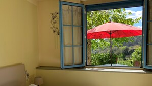 A bedroom with a bed, a window with blue shutters, and a view of greenery outside. - Comfortable cottage in a wooded area by the pool near Sarlat (Calviac-En-Périgord)