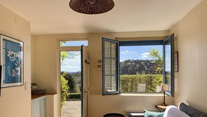 A cozy room with a bed, a small table, and a chair. There is a window with an open shutter, a door leading outside, and a framed picture on the wall. - Comfortable cottage in a wooded area by the pool near Sarlat (Calviac-En-Périgord)
