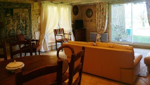 Un saló d'estar acollidor amb sostre de fusta, un sofà, una taula de dinar amb caires i una finestra gran amb cortines.