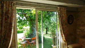 Habitació amb una gran porta corredissa de vidre que dona a un jardí. A l'interior, hi ha un sofà beix i una taula petita amb cadires.