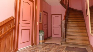 A hallway with pink walls, wooden doors, a staircase, and a chandelier. - Charming apartment in the city center of 63 m2 (Villers-sur-Mer)