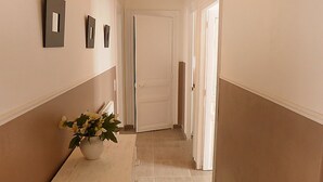 A hallway with a white door at the end, a potted plant on a counter, and three wall-mounted light switches. - Charming apartment in the city center of 63 m2 (Villers-sur-Mer)