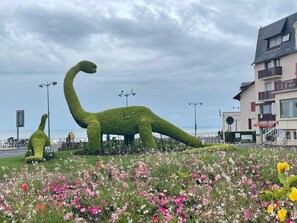 Een dinosaur vormige haag in een bloemen tuin, met een gebouw op de achtergrond.