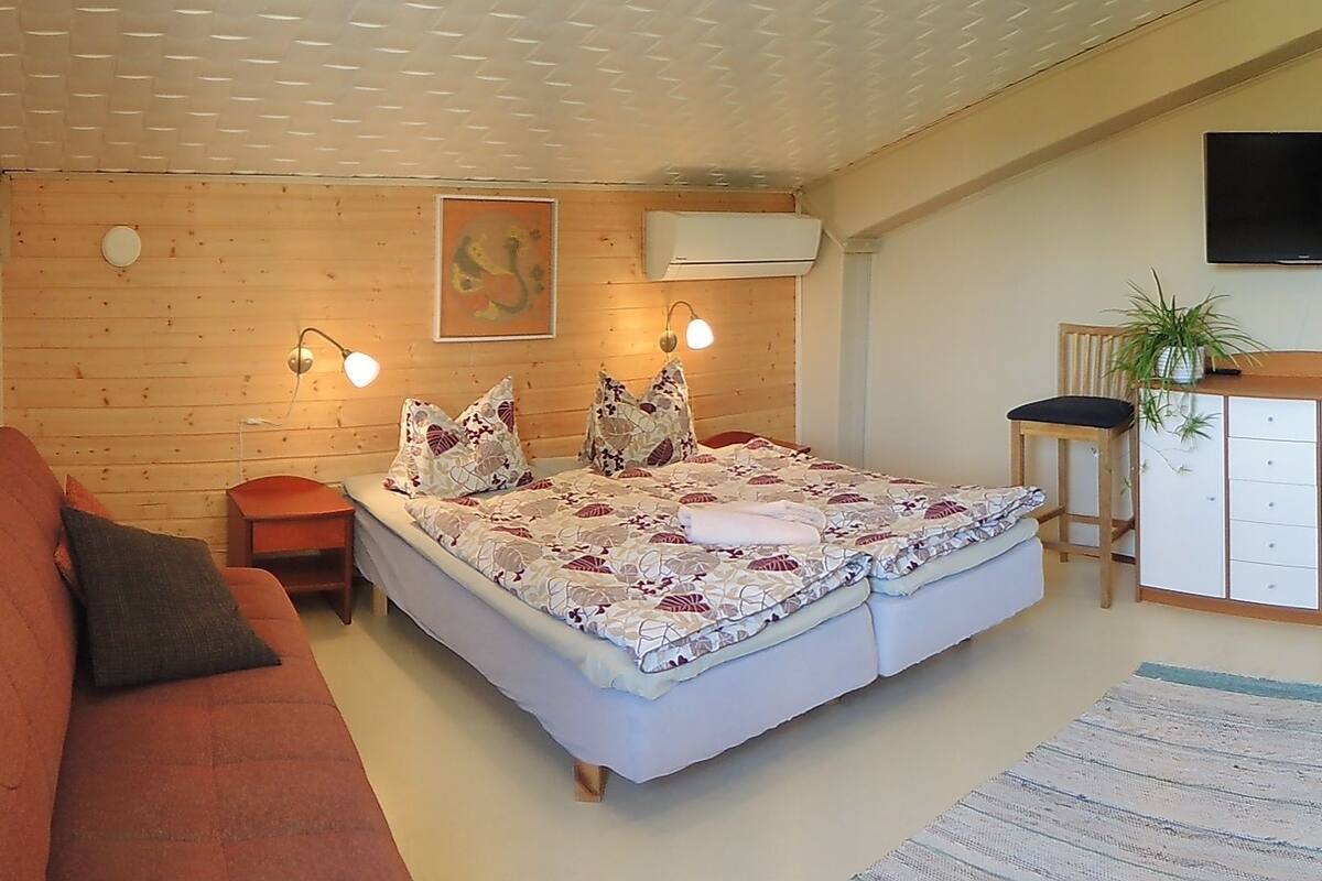 A cozy room with a bed, a sofa, a small table, a cabinet, and a TV.