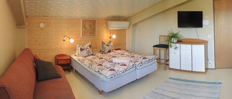 Una habitación acogedora con cama, sofá, mesita, armario y televisor.