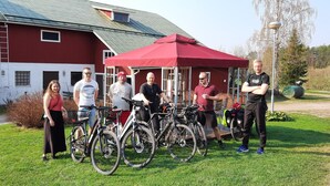 A group of people standing in front of a red barn with bicycles parked nearby.
