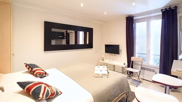 Une chambre d’hôtel avec un lit, un bureau, une chaise, une télévision et une fenêtre avec des rideaux.