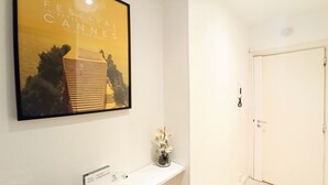 Un hall d’hôtel avec une affiche encadrée du Festival de Cannes, une console blanche ornée d’un vase de fleurs et une porte fermée.
