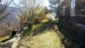 A stone building with a wooden wheel on the wall, a stone pathway, and a view of a mountain.