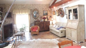 A rustic living room with exposed wooden beams, a stone wall, a sofa, a cabinet, and a television.