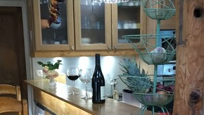 A wooden bar area with two wicker chairs, a wine bottle, and glasses on the counter.