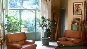 A cozy living room with a pool table, two leather chairs, and a large window offering a view of greenery.