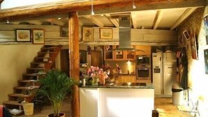 A rustic kitchen with a central island, wooden staircase, and a potted plant.
