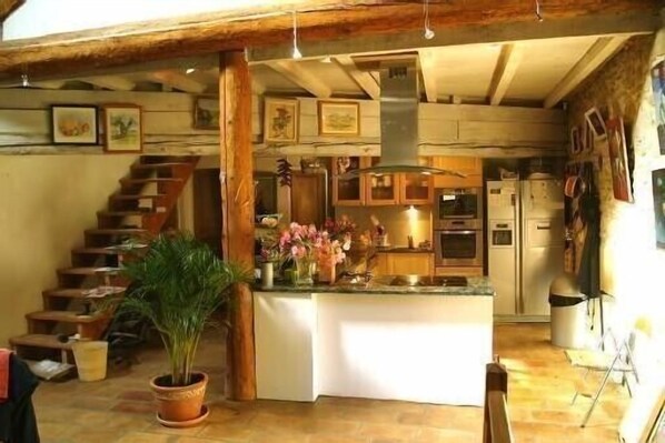 A rustic kitchen with a central island, wooden staircase, and a potted plant.