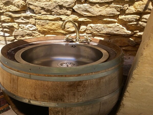 A rustic wooden barrel sink with a metal basin and a single faucet, set against a stone wall.