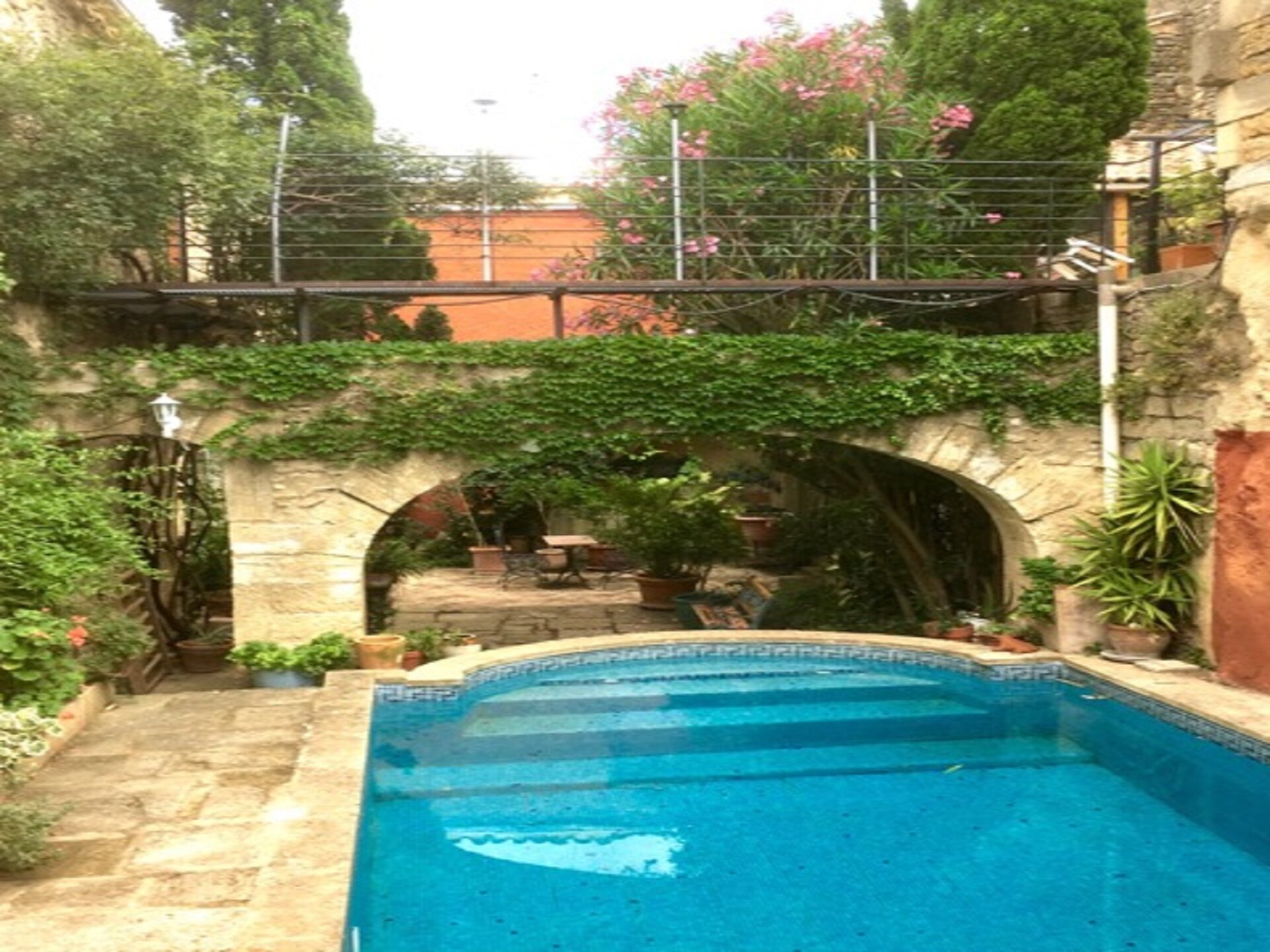 A swimming pool with a stone archway, surrounded by greenery and potted plants.