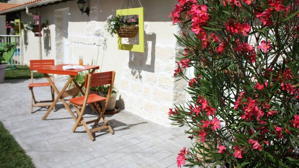 An outdoor patio with a table and chairs, a hanging plant, and a wall with a hanging basket. - GITE LACCALMIE 17 - MATHE BRILLOUET CLAUDINE ET PATRICE (Saintes)