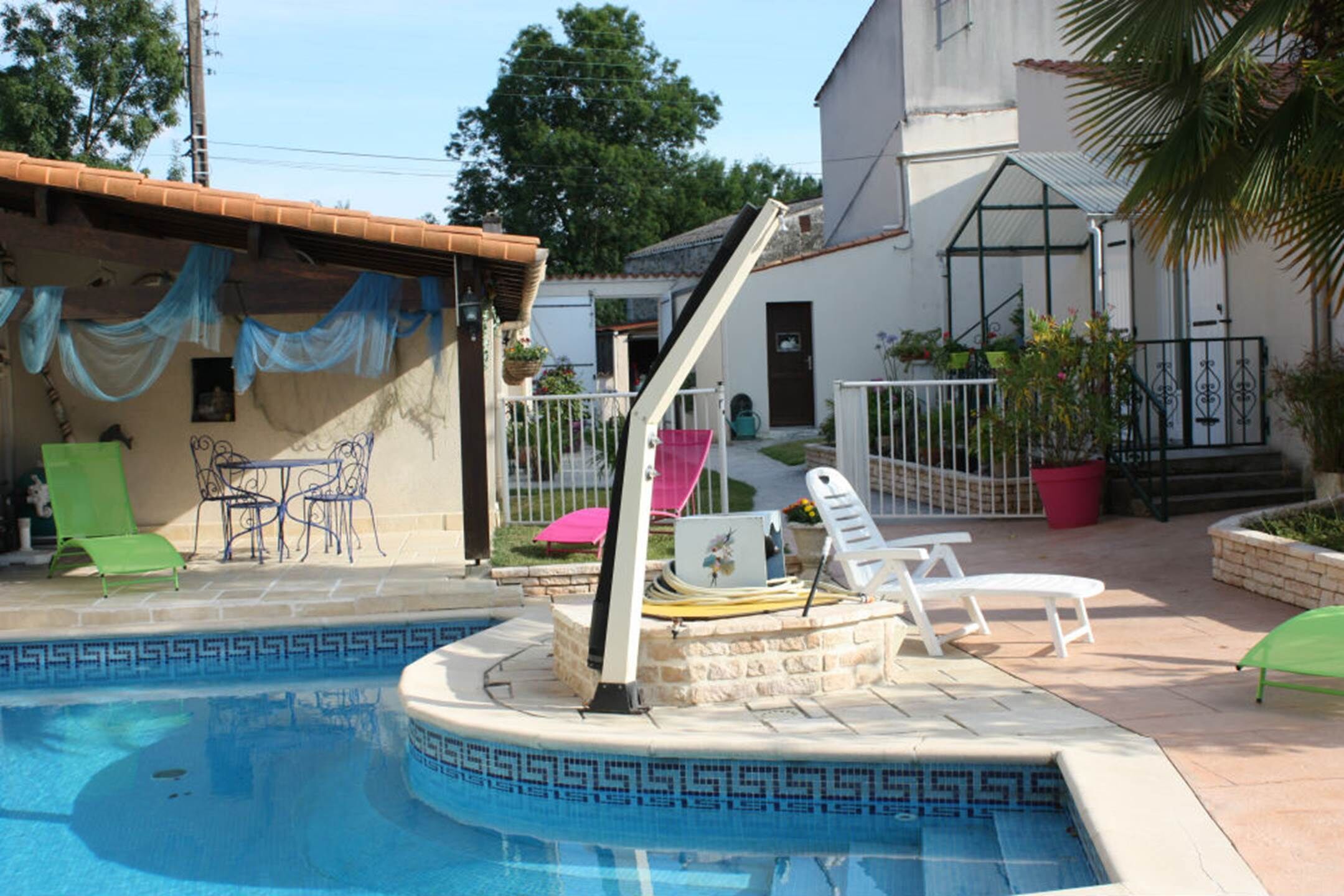 Une piscine dont le fond est recouvert de carreaux disposés selon un motif géométrique, entourée d’une terrasse aménagée avec des chaises, une table et des plantes en pot.