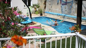 A swimming pool with two people swimming, surrounded by a white fence, with a house in the background. - GITE LACCALMIE 17 - MATHE BRILLOUET CLAUDINE ET PATRICE (Saintes)