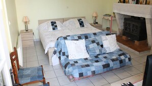 A bedroom with a bed, a chair, a nightstand, a lamp, and a fireplace. - GITE LACCALMIE 17 - MATHE BRILLOUET CLAUDINE ET PATRICE (Saintes)
