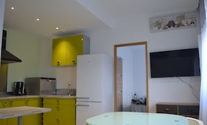 Une cuisine de taille réduite avec des meubles jaunes, un réfrigérateur blanc et une table à plateau en verre.