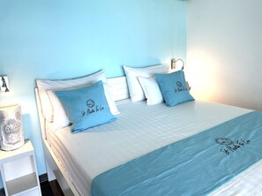 A neatly made bed with white and blue bedding, a bedside table with a lamp, and a wall-mounted light fixture.