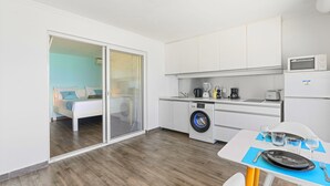 A compact hotel room with a bed, a washing machine, a kitchenette, and a dining area.