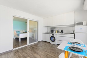 A compact hotel room with a bed, a washing machine, a kitchenette, and a dining area.