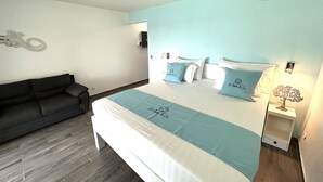 A bedroom with a bed, a dark sofa, a nightstand with a lamp, and an air conditioning unit on the wall.