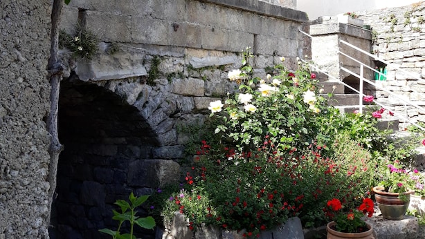 A stone building with a small archway, a staircase, and potted plants.