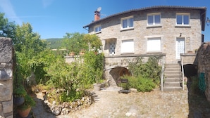 A stone house with a stone staircase leading to a door, surrounded by greenery and a clear sky.
