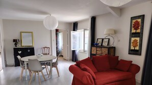 A living room with a red sofa, a dining table with chairs, a white ceiling light, and a window with curtains.