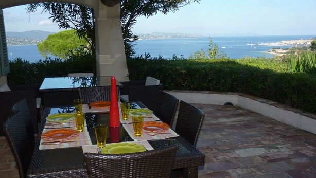 An outdoor dining area with wicker furniture and a table set for two, overlooking a scenic coastal view.