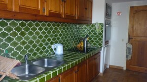 A kitchen with green patterned tiles, wooden cabinets, a stainless steel sink, and a white kettle.