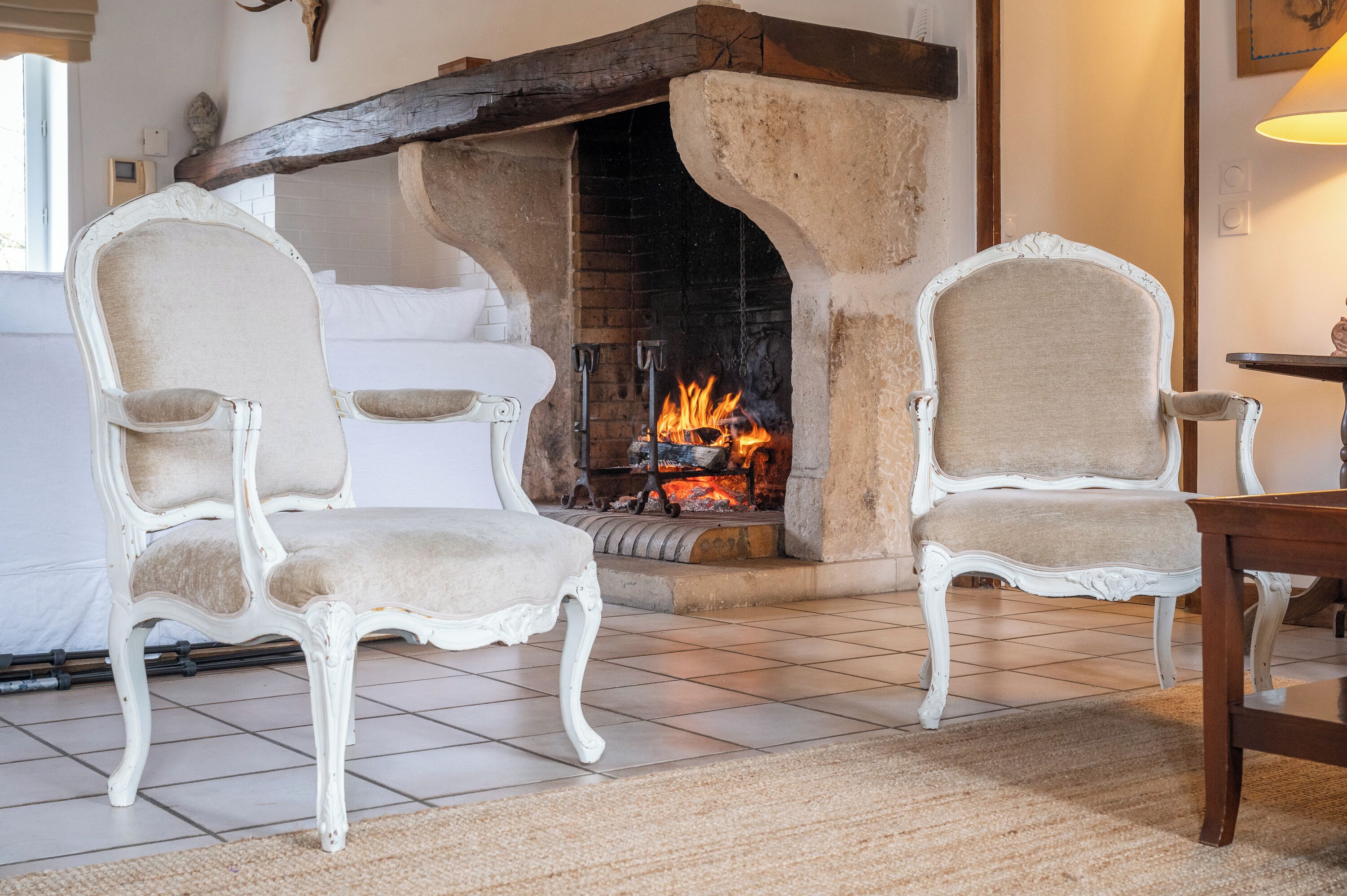Una habitación con dos sillones blancos tapizados, una chimenea con fuego a la vista y una mesa de madera.