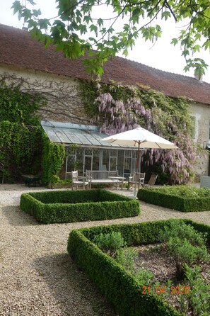 Ein Garten mit Wintergarten, ordentlich geschnittenen Hecken und einem rustikalen Gebäude.