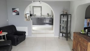 Un soggiorno moderno con un divano in pelle nera, un tavolino rotondo e una vetrina. Un arco conduce a una cucina con elettrodomestici in acciaio inossidabile e pavimento piastrellato.