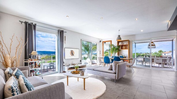 A spacious living area with a large window, a sofa, a coffee table, and a dining area with chairs. - Villa, heated pool, exceptional view, exotic garden, 4-star rating (Montbazin)
